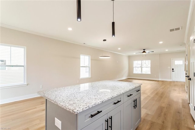 kitchen with pendant lighting, crown molding, light stone countertops, light hardwood / wood-style floors, and a kitchen island