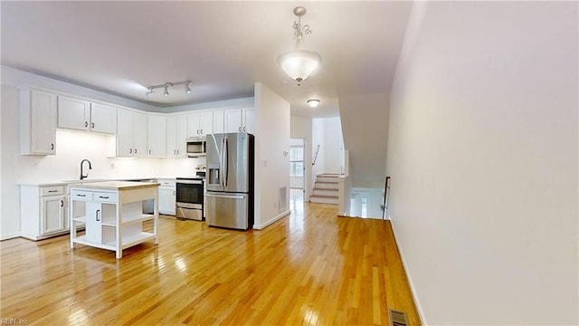 kitchen featuring sink, appliances with stainless steel finishes, white cabinetry, hanging light fixtures, and light wood-type flooring