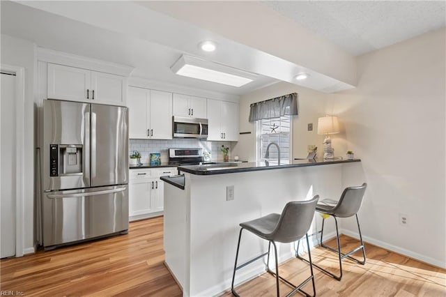 kitchen with white cabinetry, a kitchen bar, kitchen peninsula, and appliances with stainless steel finishes