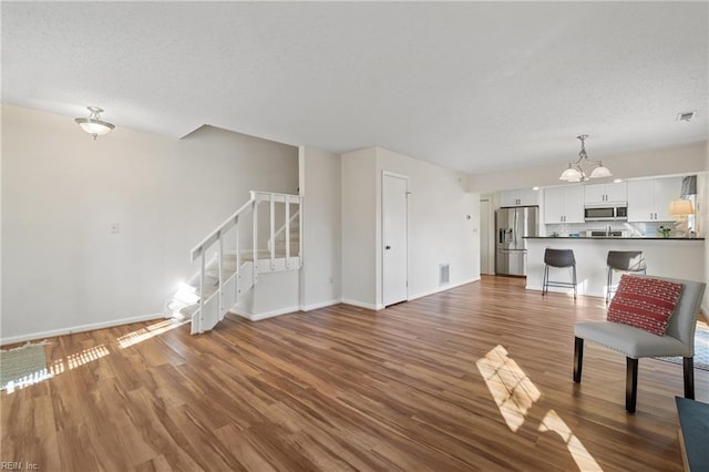 unfurnished living room featuring hardwood / wood-style flooring, a textured ceiling, and an inviting chandelier