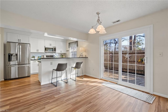 kitchen featuring a breakfast bar area, hanging light fixtures, stainless steel appliances, white cabinets, and kitchen peninsula