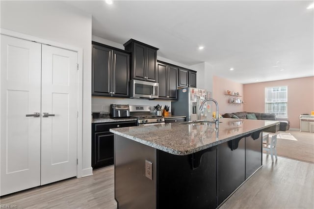 kitchen featuring sink, appliances with stainless steel finishes, a kitchen island with sink, a kitchen bar, and light wood-type flooring