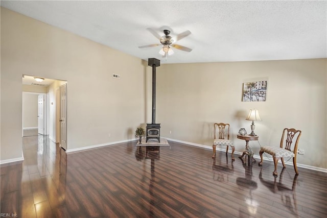 sitting room featuring lofted ceiling, a wood stove, dark wood-type flooring, and ceiling fan