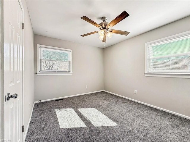 empty room featuring ceiling fan, a wealth of natural light, and dark colored carpet