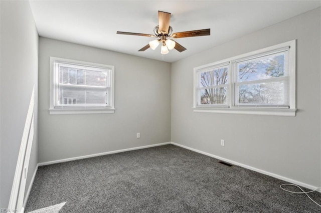 empty room with a wealth of natural light, ceiling fan, and dark colored carpet