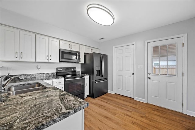 kitchen featuring sink, white cabinetry, stainless steel appliances, dark stone counters, and light wood-type flooring