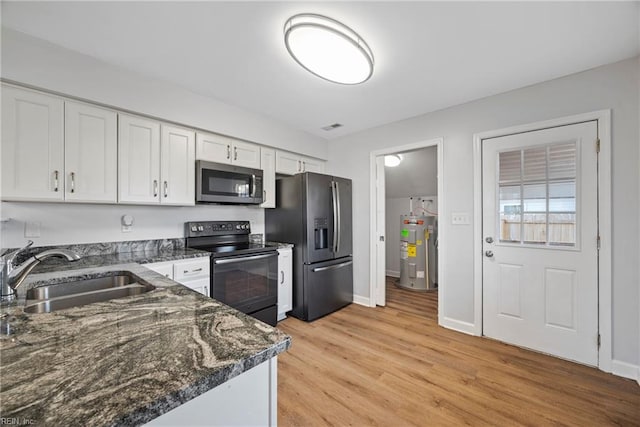 kitchen with appliances with stainless steel finishes, water heater, sink, white cabinets, and light hardwood / wood-style floors