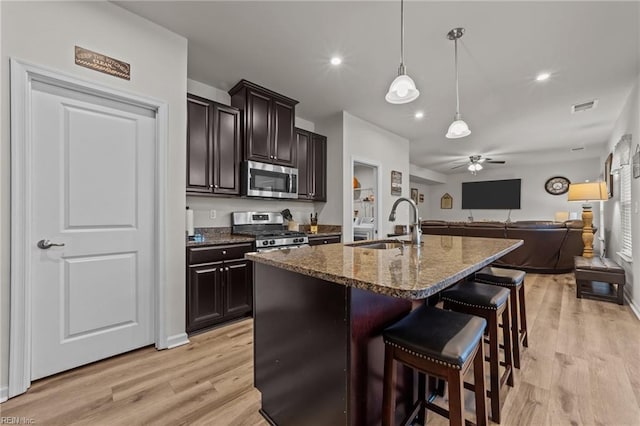 kitchen featuring sink, appliances with stainless steel finishes, a kitchen bar, dark brown cabinetry, and stone countertops