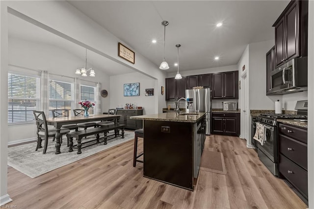 kitchen featuring decorative light fixtures, appliances with stainless steel finishes, a kitchen breakfast bar, an island with sink, and dark stone counters