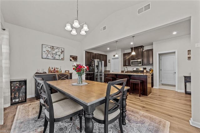 dining space with wine cooler, lofted ceiling, sink, a notable chandelier, and light hardwood / wood-style floors