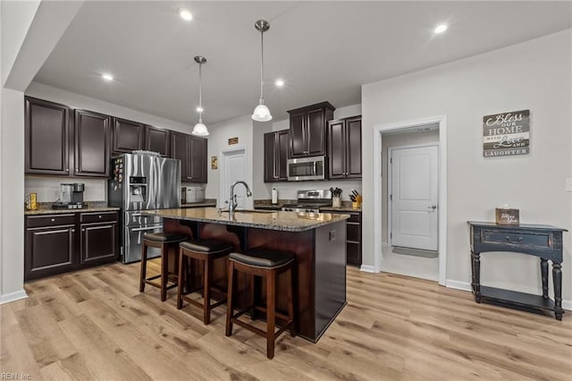 kitchen featuring sink, a breakfast bar area, appliances with stainless steel finishes, a kitchen island with sink, and hanging light fixtures