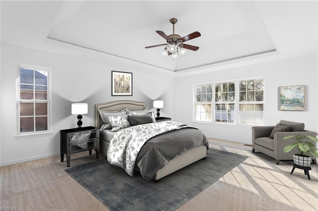 carpeted bedroom featuring multiple windows, a tray ceiling, and ceiling fan