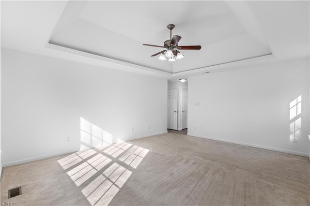 spare room featuring ceiling fan, light colored carpet, and a raised ceiling