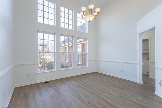 spare room featuring hardwood / wood-style flooring, a towering ceiling, and a notable chandelier