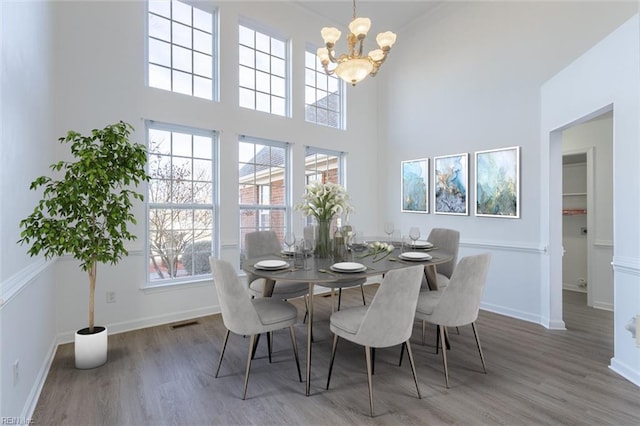 dining space with a high ceiling, wood-type flooring, and an inviting chandelier