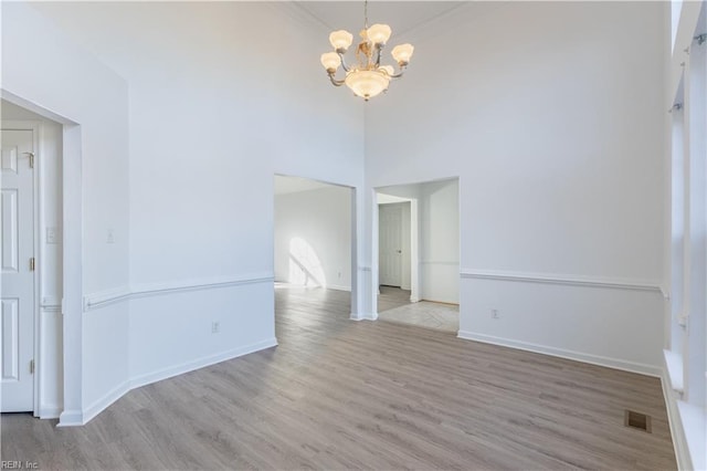 spare room featuring a towering ceiling, light hardwood / wood-style flooring, and a notable chandelier