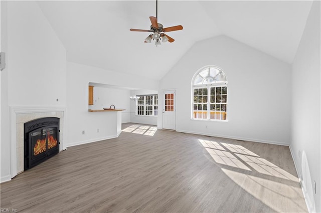 unfurnished living room featuring a tile fireplace, ceiling fan with notable chandelier, hardwood / wood-style floors, and high vaulted ceiling