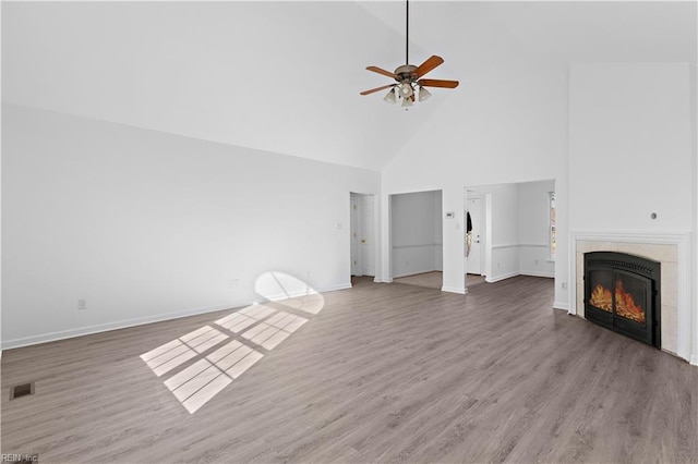 unfurnished living room featuring hardwood / wood-style flooring, a tile fireplace, high vaulted ceiling, and ceiling fan