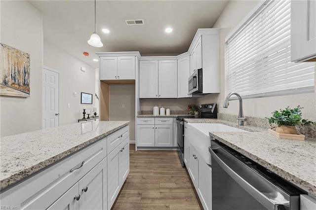 kitchen featuring light stone counters, decorative light fixtures, hardwood / wood-style flooring, stainless steel appliances, and white cabinets