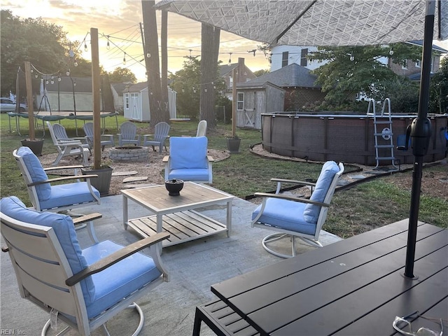 patio terrace at dusk with a storage shed, a trampoline, and an outdoor fire pit