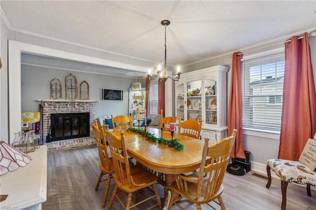 dining room with crown molding, wood-type flooring, a notable chandelier, and a fireplace