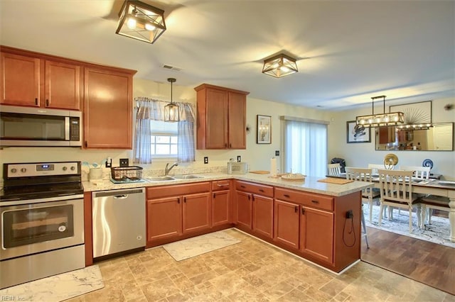 kitchen with decorative light fixtures, sink, kitchen peninsula, stainless steel appliances, and light stone countertops