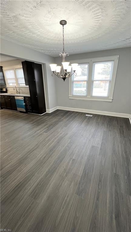 unfurnished dining area featuring dark wood-type flooring, sink, a textured ceiling, and a chandelier