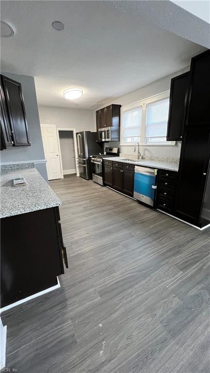 kitchen with light stone counters, sink, light hardwood / wood-style floors, and appliances with stainless steel finishes