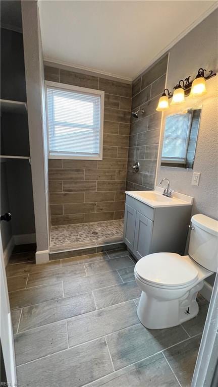 bathroom featuring crown molding, vanity, toilet, and a tile shower