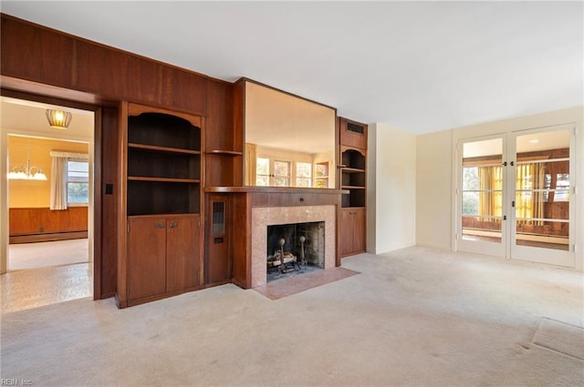 unfurnished living room featuring a tile fireplace, wooden walls, light colored carpet, baseboard heating, and french doors