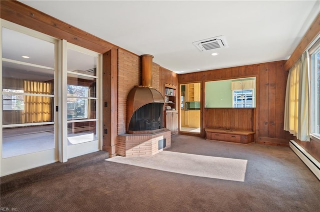 unfurnished living room featuring dark colored carpet, a baseboard radiator, a wood stove, and wooden walls