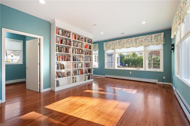 workout room featuring hardwood / wood-style flooring, a healthy amount of sunlight, and a baseboard heating unit