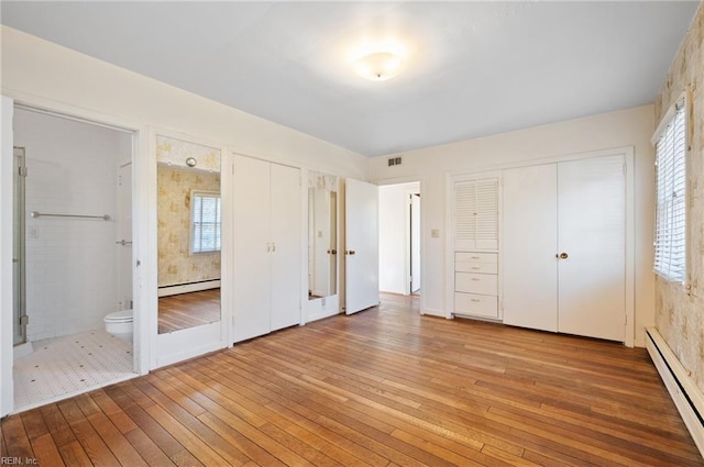 unfurnished bedroom with hardwood / wood-style flooring, a baseboard heating unit, multiple closets, and multiple windows