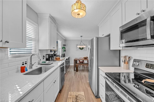 kitchen with sink, decorative light fixtures, light wood-type flooring, appliances with stainless steel finishes, and white cabinets