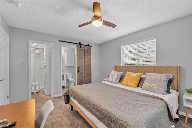 carpeted bedroom featuring a walk in closet, ensuite bath, a textured ceiling, a closet, and a barn door