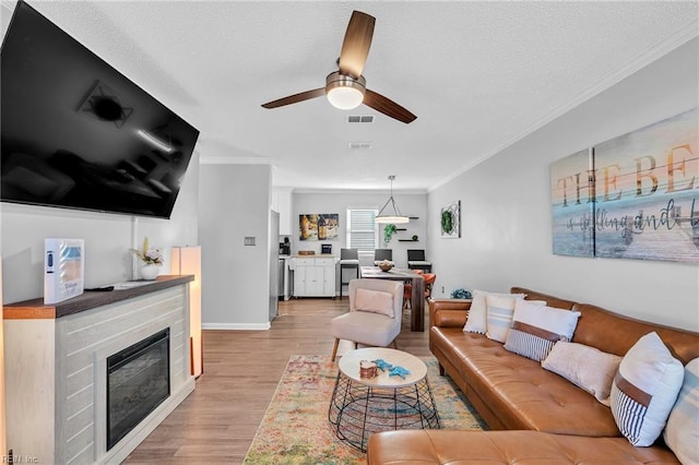 living room with crown molding, a textured ceiling, ceiling fan, and light hardwood / wood-style flooring