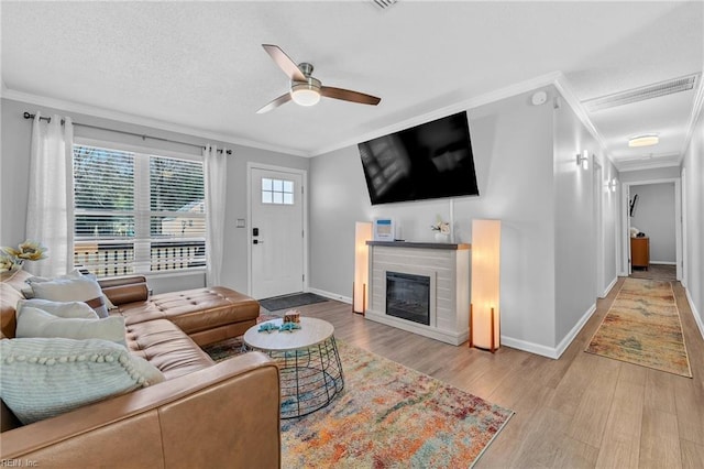 living room featuring ceiling fan, ornamental molding, light hardwood / wood-style floors, and a textured ceiling