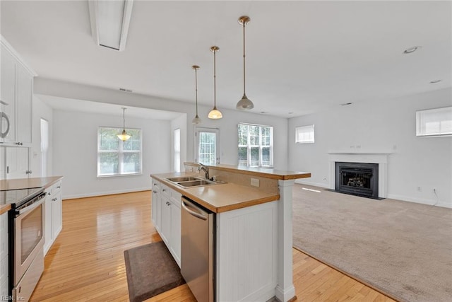 kitchen featuring sink, appliances with stainless steel finishes, hanging light fixtures, an island with sink, and white cabinets