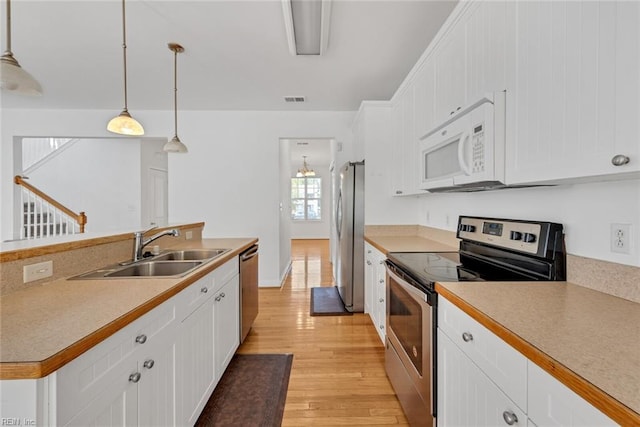 kitchen with hanging light fixtures, white cabinetry, appliances with stainless steel finishes, and sink