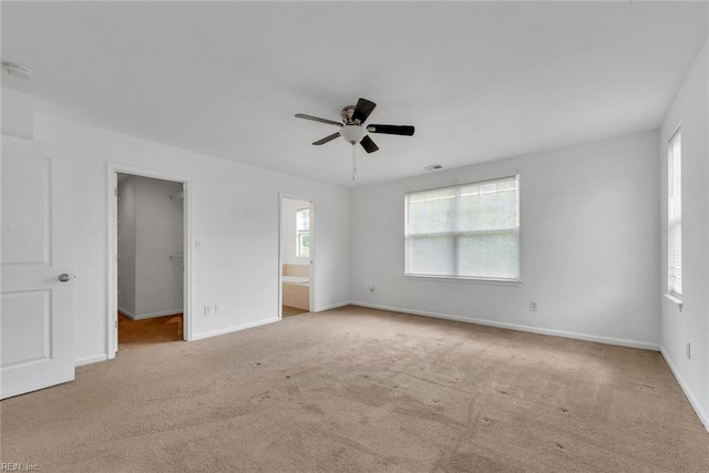 unfurnished bedroom featuring connected bathroom, a walk in closet, light colored carpet, ceiling fan, and a closet