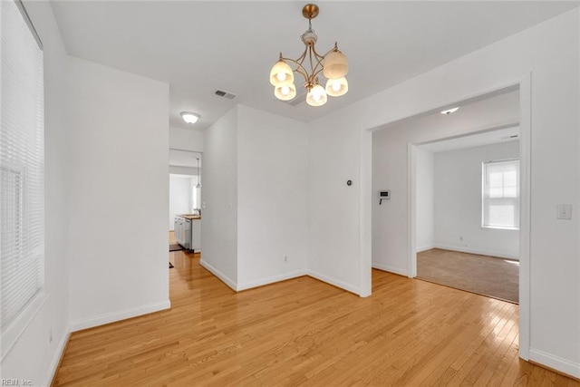 unfurnished dining area with an inviting chandelier and light wood-type flooring