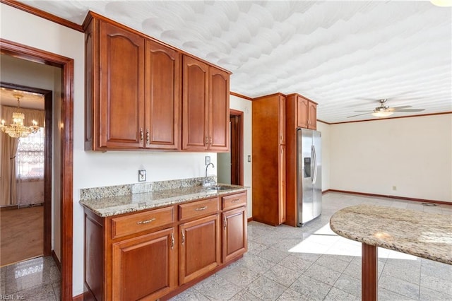 kitchen with crown molding, stainless steel fridge, light stone countertops, and sink