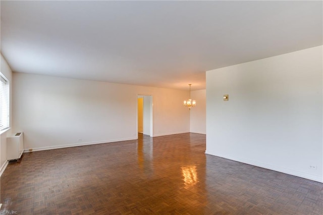 empty room featuring dark parquet flooring, radiator, and a notable chandelier