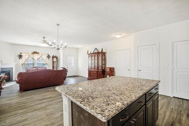 kitchen with dark brown cabinets, a center island, light stone counters, light hardwood / wood-style floors, and decorative light fixtures