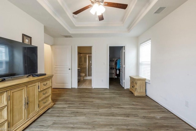 bedroom featuring ensuite bathroom, crown molding, a spacious closet, a tray ceiling, and hardwood / wood-style flooring