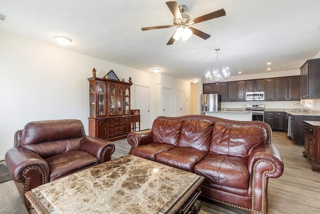 living room featuring ceiling fan with notable chandelier, sink, and light hardwood / wood-style floors