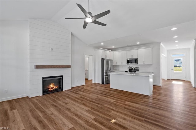 kitchen featuring white cabinetry, a large fireplace, appliances with stainless steel finishes, dark hardwood / wood-style floors, and an island with sink