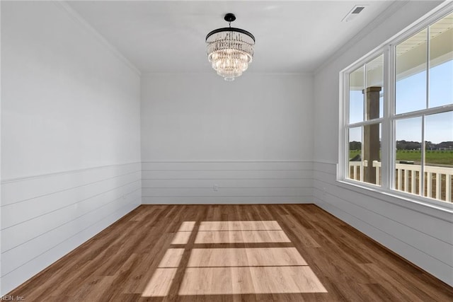 unfurnished room featuring hardwood / wood-style flooring, ornamental molding, and an inviting chandelier