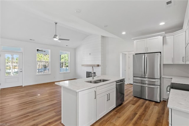 kitchen with appliances with stainless steel finishes, lofted ceiling, sink, white cabinets, and light stone countertops