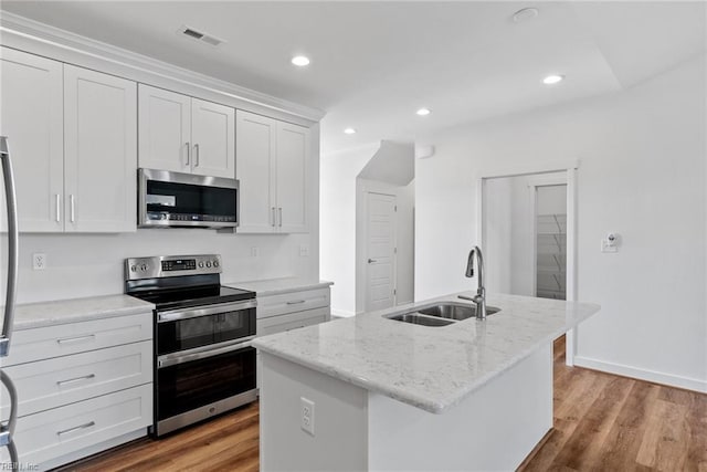 kitchen with sink, appliances with stainless steel finishes, light stone counters, an island with sink, and white cabinets